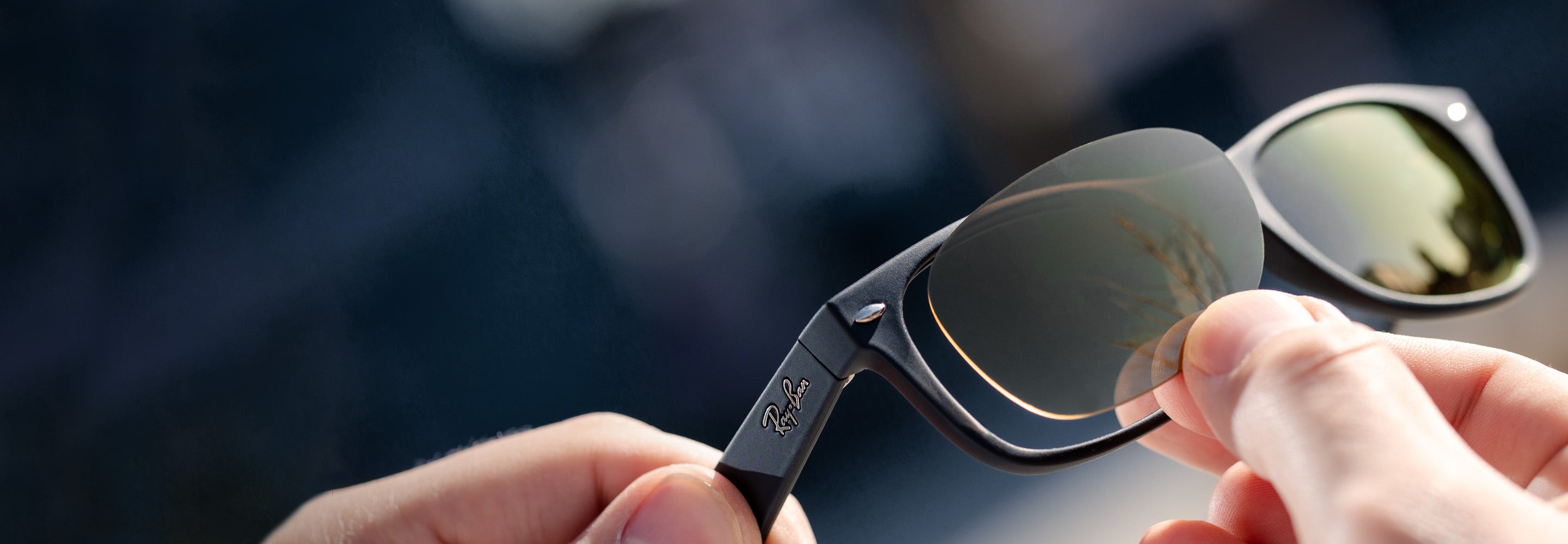 Close-up of hands holding a pair of Ray-Ban sunglasses with reflective green lenses.